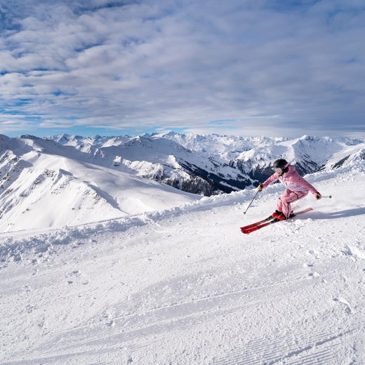 Mädchen fährt die Piste runter in einem pinken Skianzug | © Bergbahnen Fieberbrunn